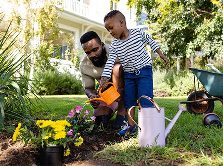 Person and child watering plants in front yard