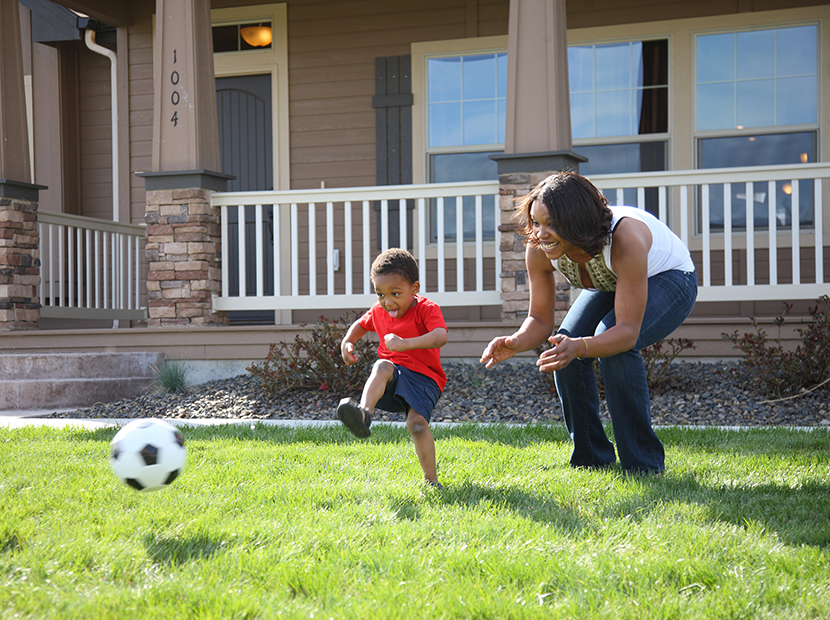 A mother and son play soccer in their front yard