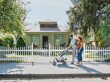 Mom and dad pushing stroller on a walk in front of a house