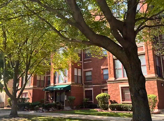 Outside view of a red brick apartment building with two trees in front