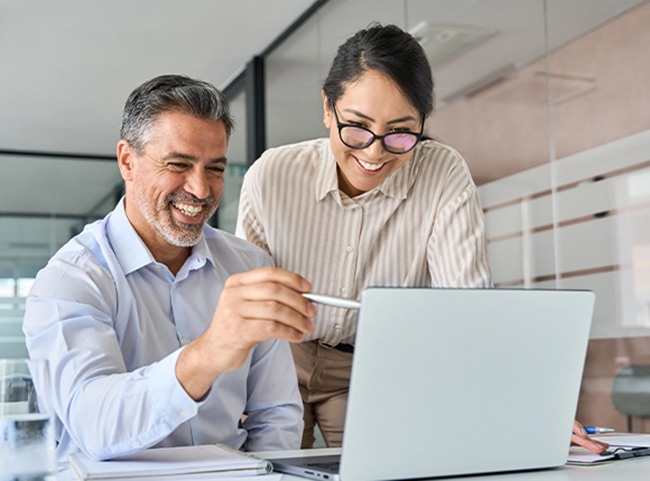 Smiling man and women dressed in professional clothing lean over a laptop together