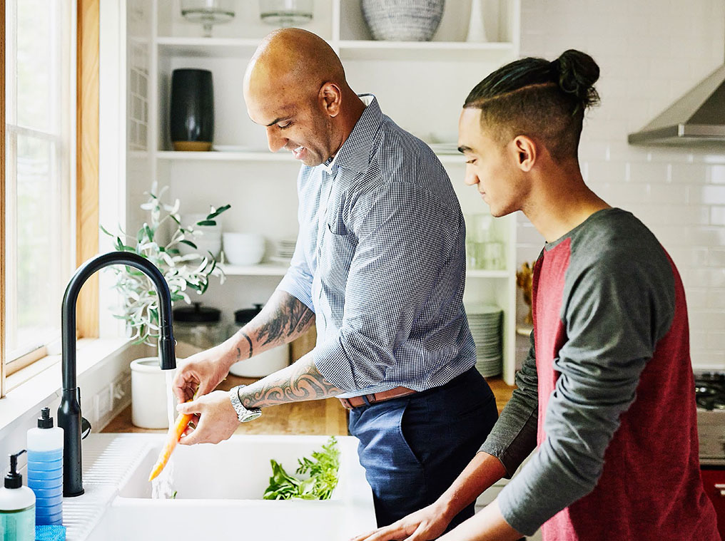 Two people washing vegetables at kitchen sink